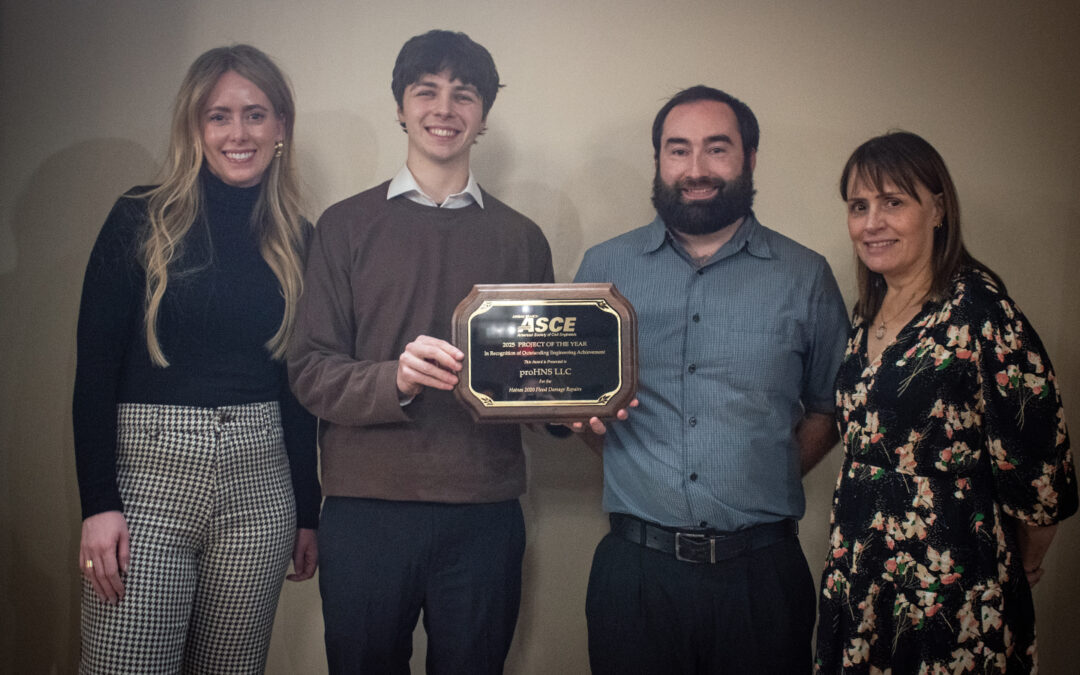 Four employees stand shoulder to shoulder on a stage holding an award plaque.