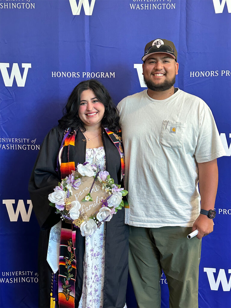 A woman is standing next to a man posing with her cap and gown at a university graduation ceremony.