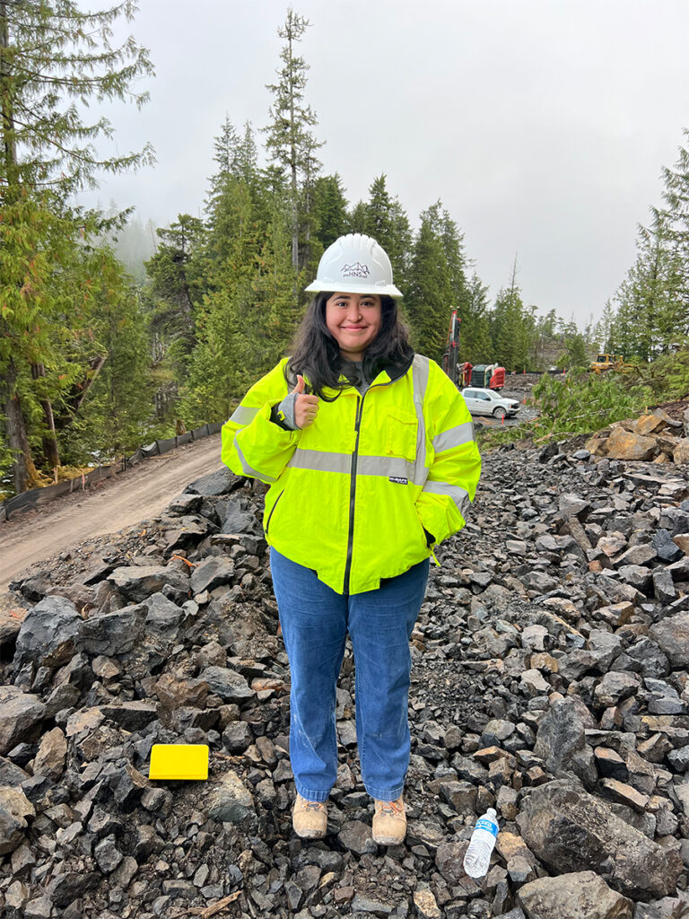 A female engineer standing on a rock pile at a job site in remote Alaska.
