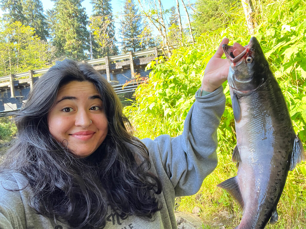 A woman is holding a salmon that she caught and smiling.